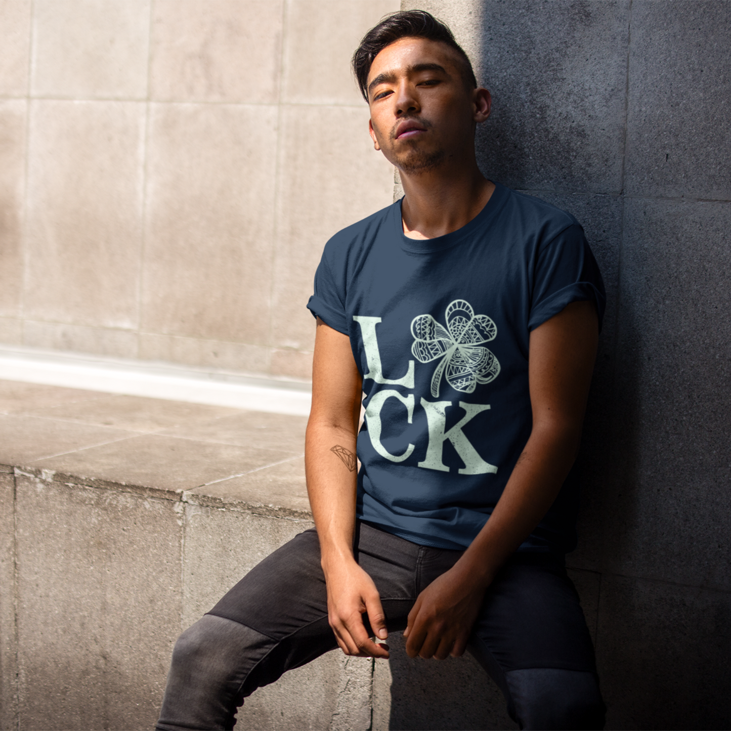 Man wearing a blue t-shirt with a graphic design leaning against a wall.