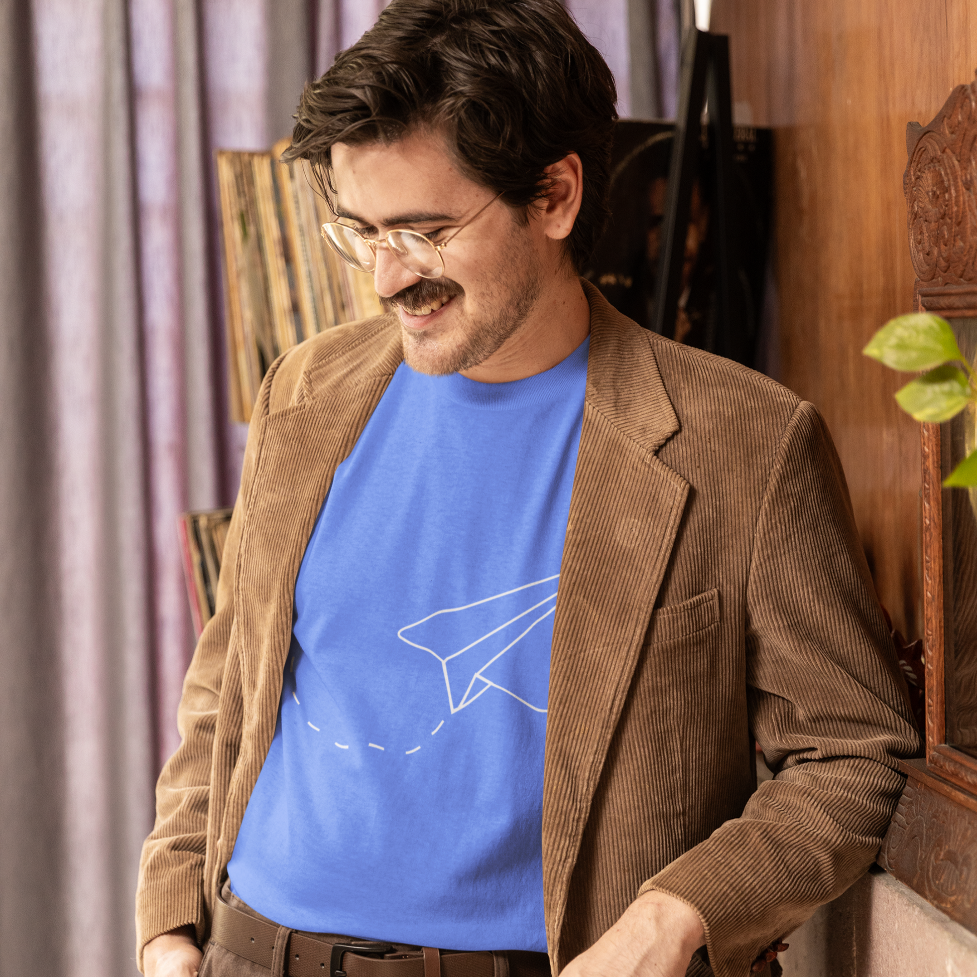 Man wearing a brown blazer over a blue shirt with a graphic design, standing indoors.