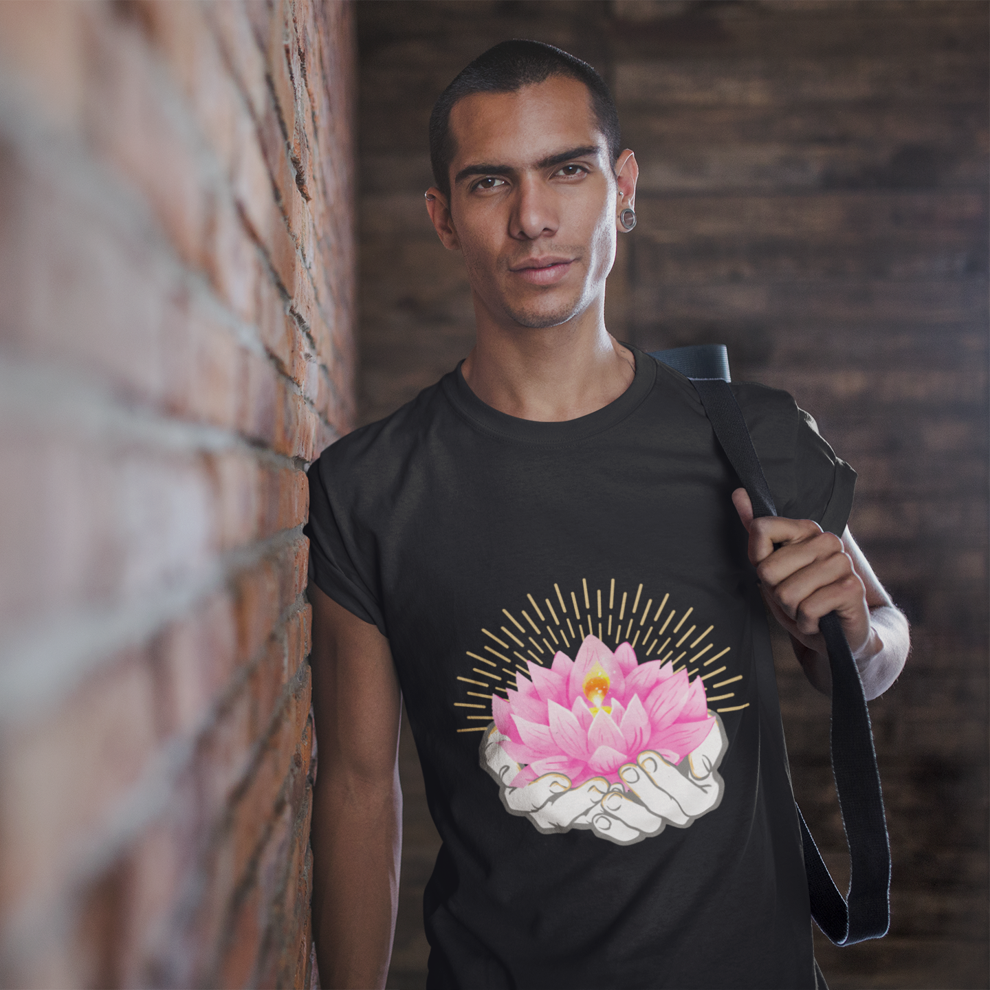 Man wearing a black t-shirt with a pink flower design, leaning against a brick wall.