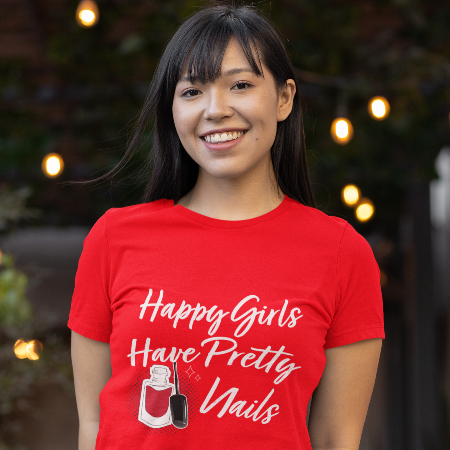 Person wearing a red t-shirt with a nail polish graphic and text, standing outdoors with lights in the background.