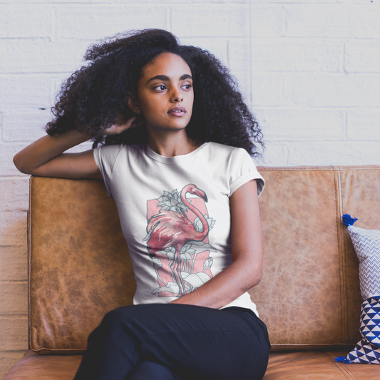 Woman sitting on a brown couch wearing a white t-shirt with a flamingo design, against a light brick wall.