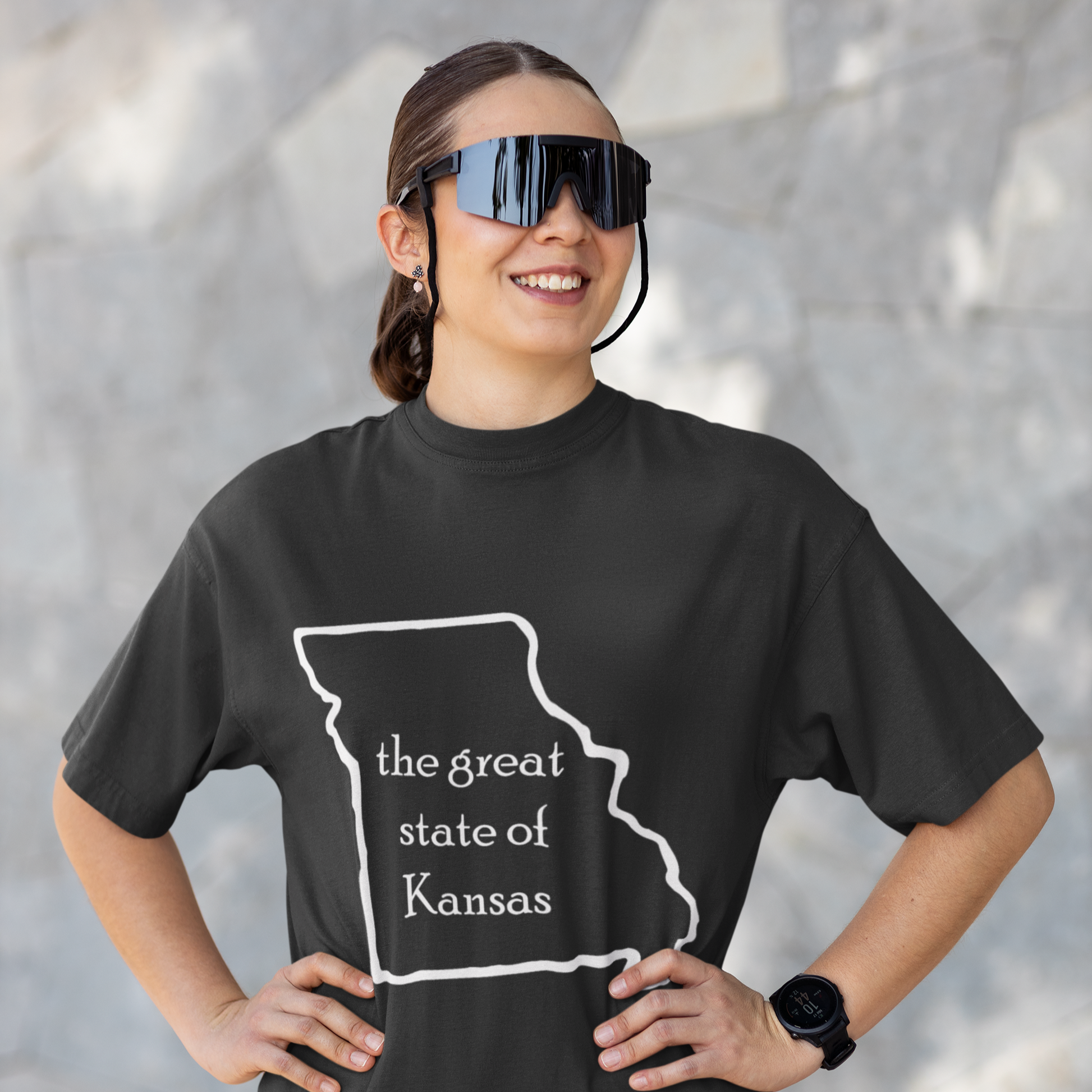 Person wearing a black t-shirt with 'the great state of Kansas' design, standing against a gray wall.