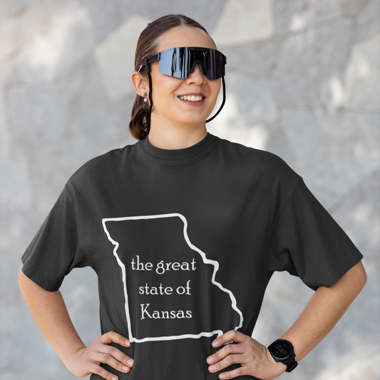 Person wearing a black t-shirt with 'the great state of Kansas' design, standing against a gray wall.