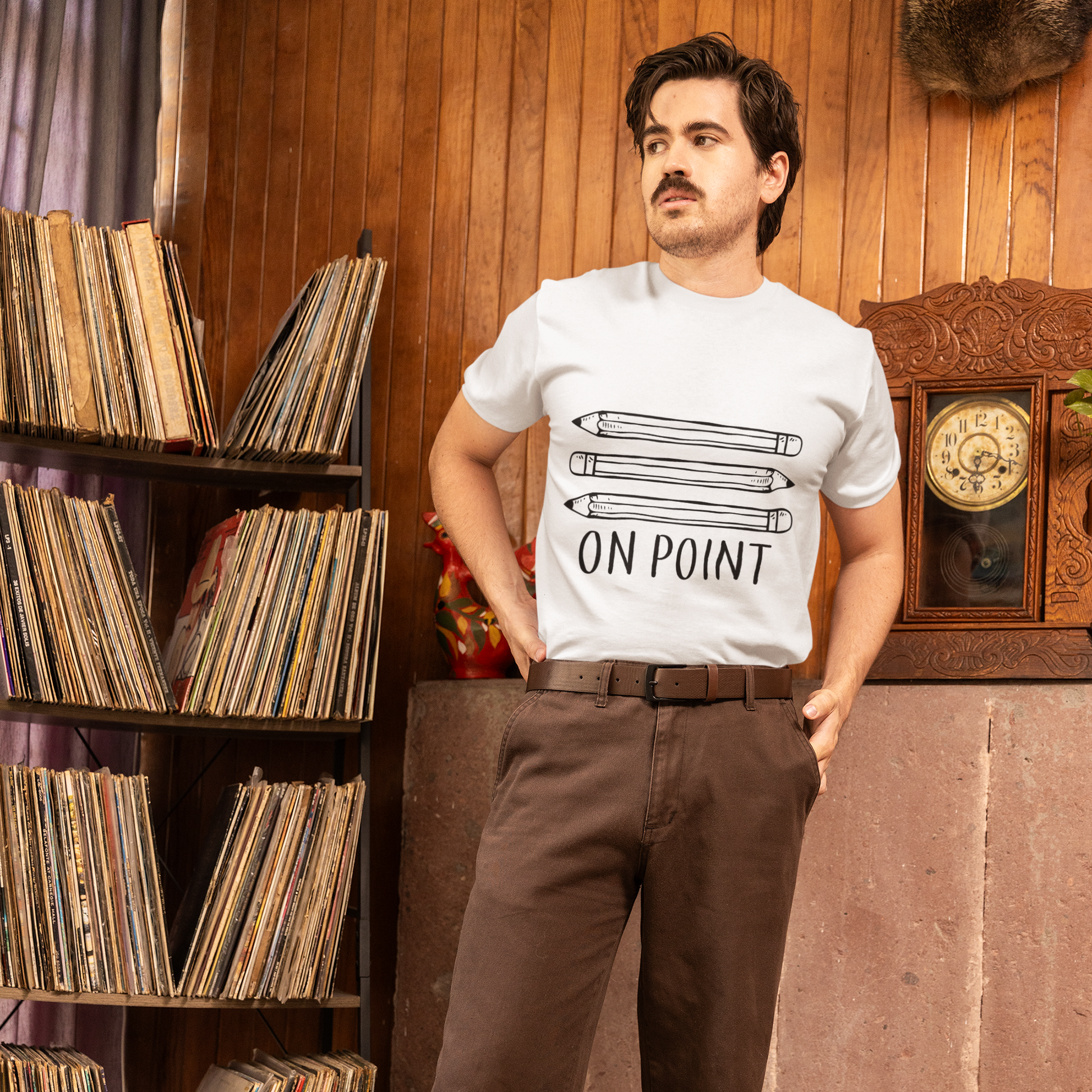 Man wearing a white t-shirt with text standing in a room with vinyl records and a clock.
