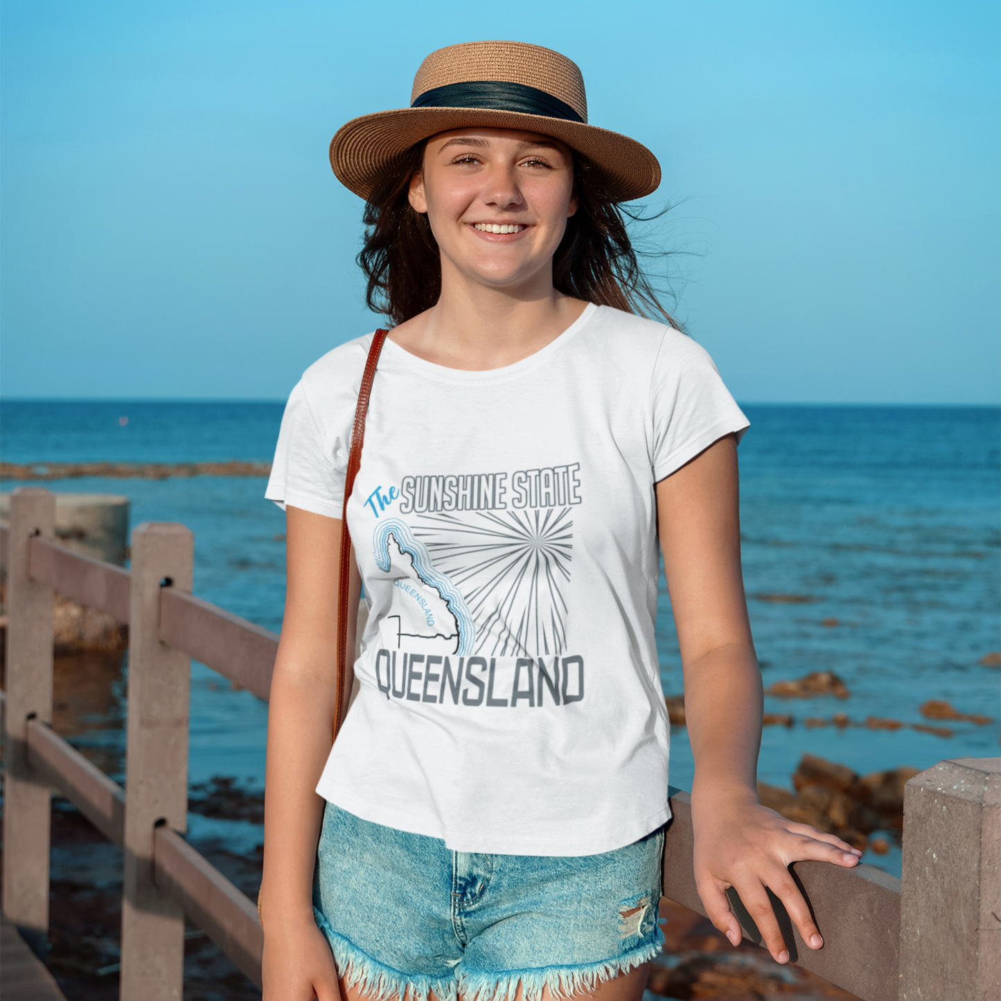 Person wearing a 'Sunshine State Queensland' t-shirt by the ocean