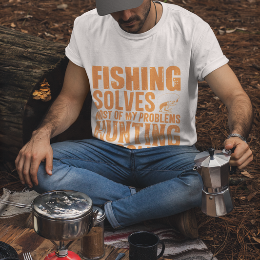 Man sitting outdoors with camping gear and a coffee maker, wearing a t-shirt with text.