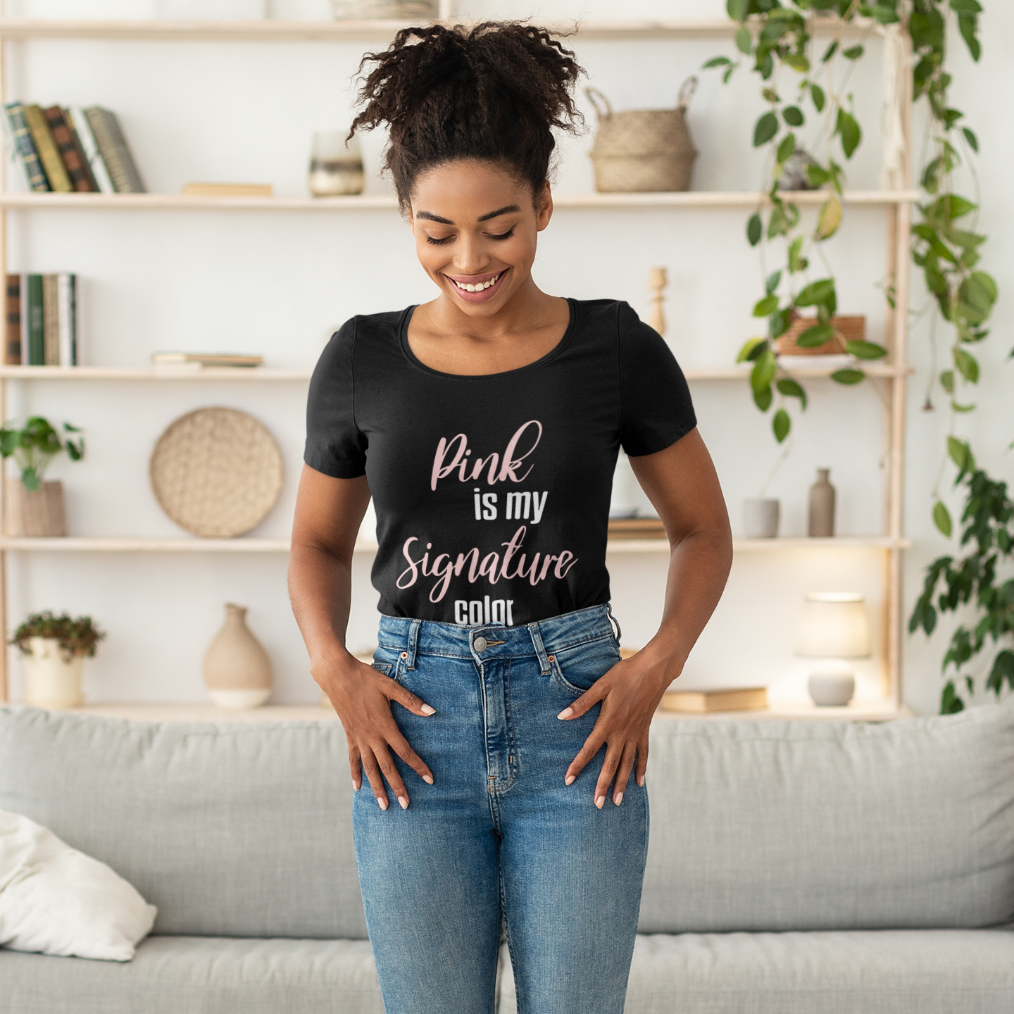 Woman standing on a scale in a living room wearing a black t-shirt with text and blue jeans.