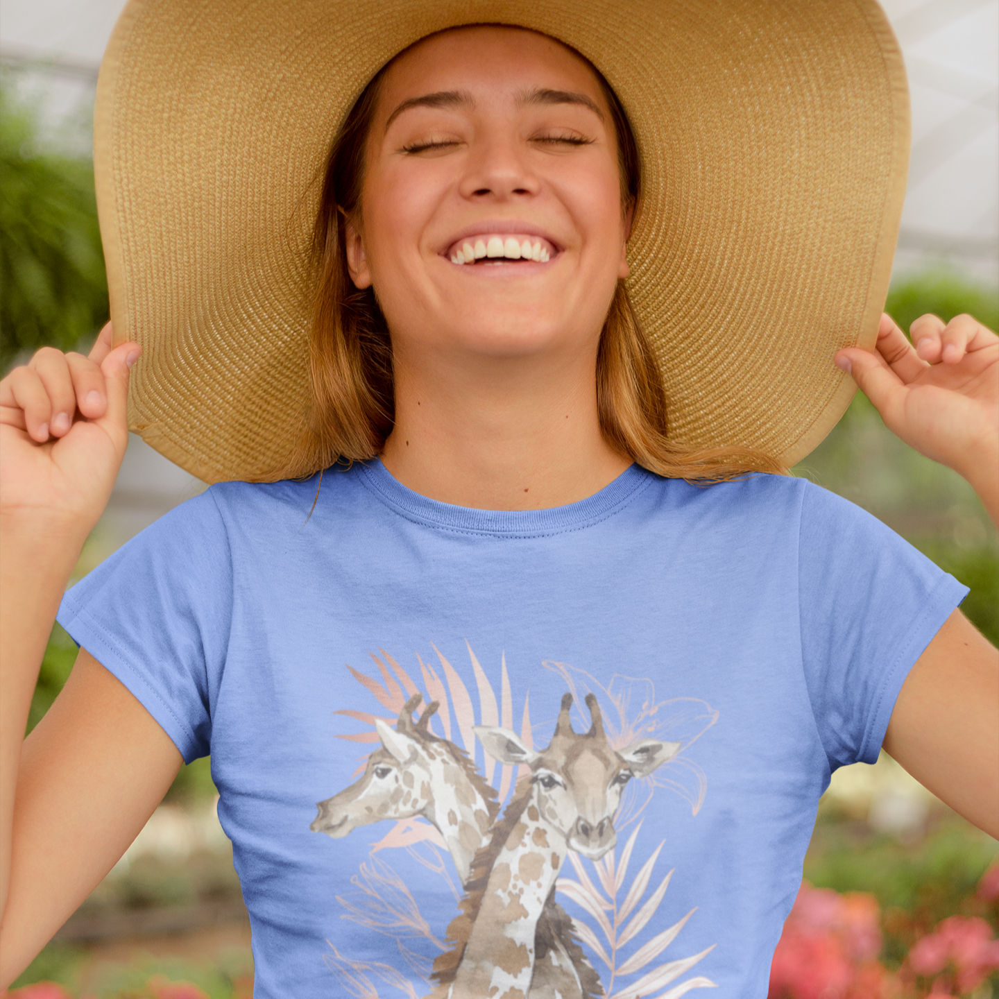 Woman wearing a blue t-shirt with giraffe design and a wide-brimmed hat, standing outdoors.