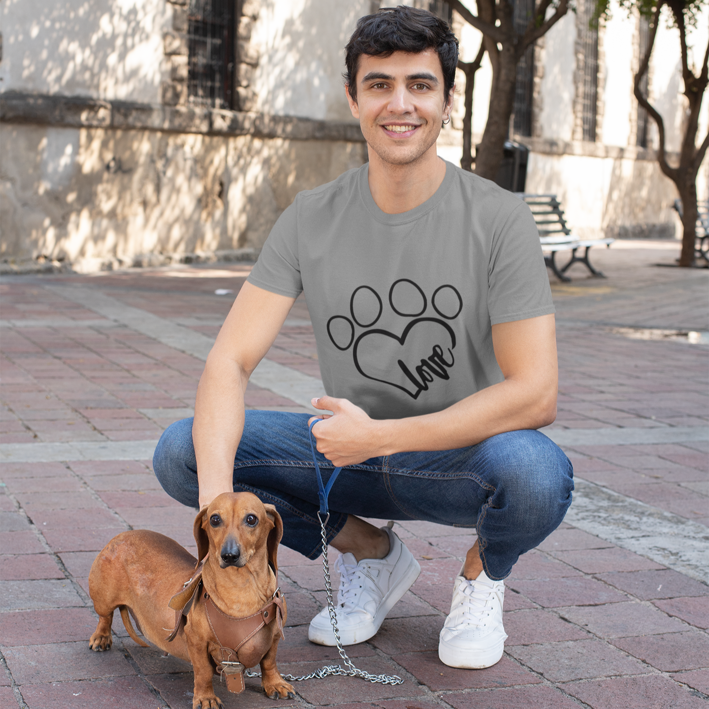 Man squatting with a small dog on a leash in an outdoor setting
