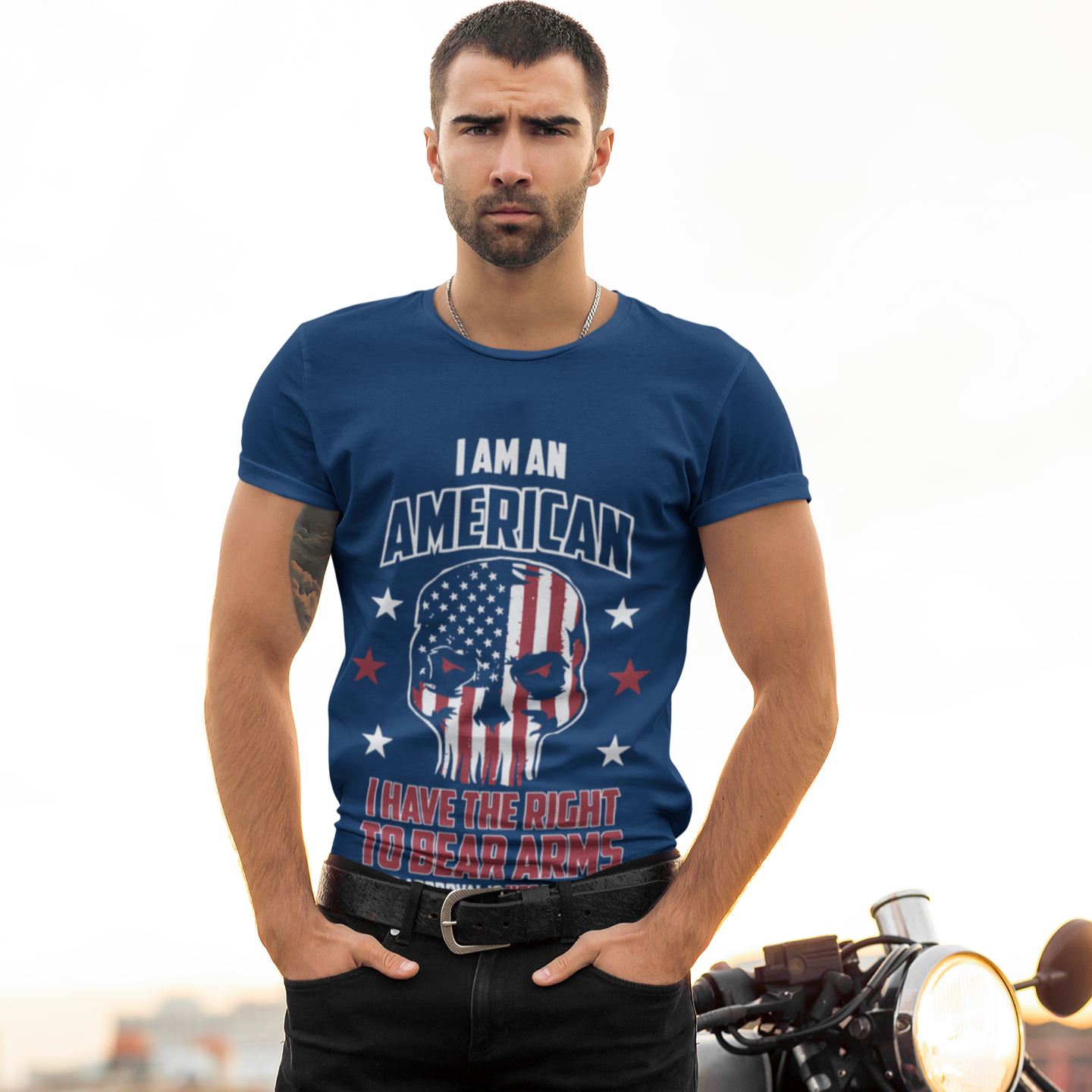 Man wearing a blue t-shirt with a graphic design standing next to a motorcycle.