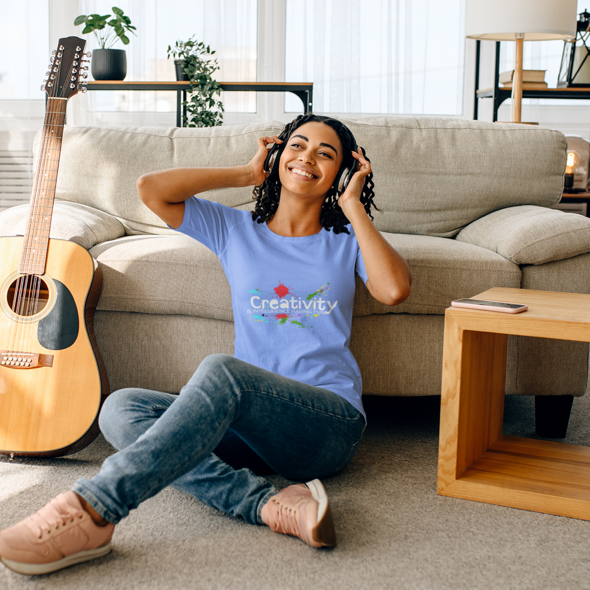 Person sitting on the floor with a guitar and headphones, wearing a blue t-shirt with 'Creativity' printed on it.