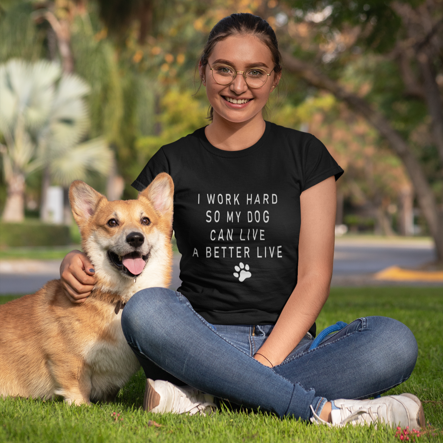 Woman sitting on grass with a dog, wearing a black t-shirt with text.