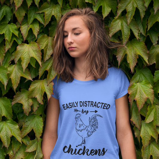 Woman wearing a blue t-shirt with a chicken graphic and text, standing against a leafy background.